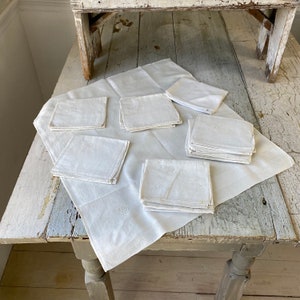 Peut inclure: Un lot de serviettes en lin blanc avec des initiales brodées. Les serviettes sont disposées sur une table en bois blanc.