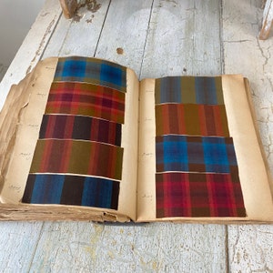 May include: An open book with fabric swatches of different plaid patterns in shades of red, brown, blue, and green. The book is labeled with the word "Sample" on each page.