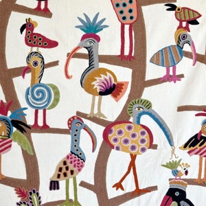 May include: A white fabric wall hanging with colorful embroidered birds. The birds are stylized and have different patterns and colors. The background is white with brown stitching.