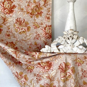 Könnte beinhalten: Ein beigefarbener Stoff mit einem floralen Muster in Orange-, Rosa- und Brauntönen. Der Stoff ist über einen weißen Holzsockel gelegt.