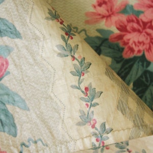 K&ouml;nnte beinhalten: Eine Nahaufnahme eines Stoffes mit einem Blumenmuster. Der Stoff ist beige mit einem sich wiederholenden Muster aus rosa Bl&uuml;ten und gr&uuml;nen Bl&auml;ttern. Der Stoff ist leicht verblasst und hat einen Vintage-Look.