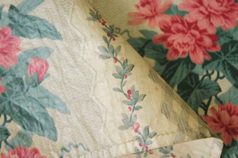 K&ouml;nnte beinhalten: Eine Nahaufnahme eines Stoffes mit einem Blumenmuster. Der Stoff ist beige mit einem sich wiederholenden Muster aus rosa Bl&uuml;ten und gr&uuml;nen Bl&auml;ttern. Der Stoff ist leicht verblasst und hat einen Vintage-Look.