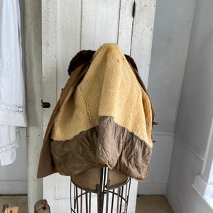 May include: A brown leather jacket with a shearling lining. The jacket is turned inside out to show the lining. The jacket is on a mannequin.