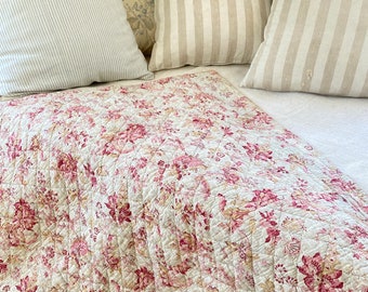 May include: A white quilted bedspread with a floral pattern in shades of pink and red. The bedspread is made of cotton and has a soft, comfortable feel.