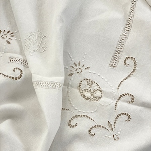 Pode incluir: Toalha de mesa de linho branco com delicados desenhos florais e de volutas bordados. A toalha de mesa apresenta uma inicial "A" bordada no canto superior esquerdo.