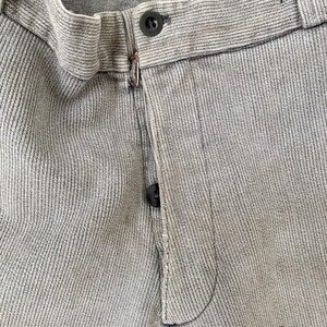 May include: Close-up of the front of a pair of gray pants with a button fly and a single button closure. The pants have a textured, ribbed fabric.