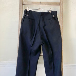 May include: Black tailored pants with a pleated front and a belt loop detail. The pants have a straight leg and a classic fit.