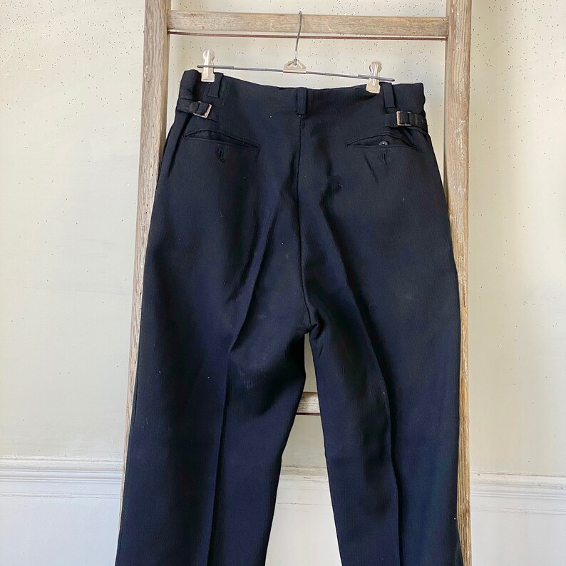 May include: Black tailored pants with a pleated front and a belt loop detail. The pants have a straight leg and a classic fit.