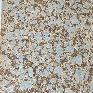 May include: Close-up of a marbled paper design. The pattern features a mix of light blue and brown organic shapes, creating a textured, mottled appearance. The paper has a vintage aesthetic, with a light blue edge.