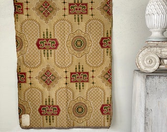 Peut inclure: Un tissu beige avec un motif répétitif de formes géométriques rouges, vertes et dorées. Le tissu a une texture tissée et est encadré par une bordure brune.
