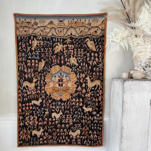 May include: A tapestry with a black background and a colorful design. The design features a central crest with a shield and a crown, surrounded by stylized flowers, birds, and deer. The tapestry has a brown border.