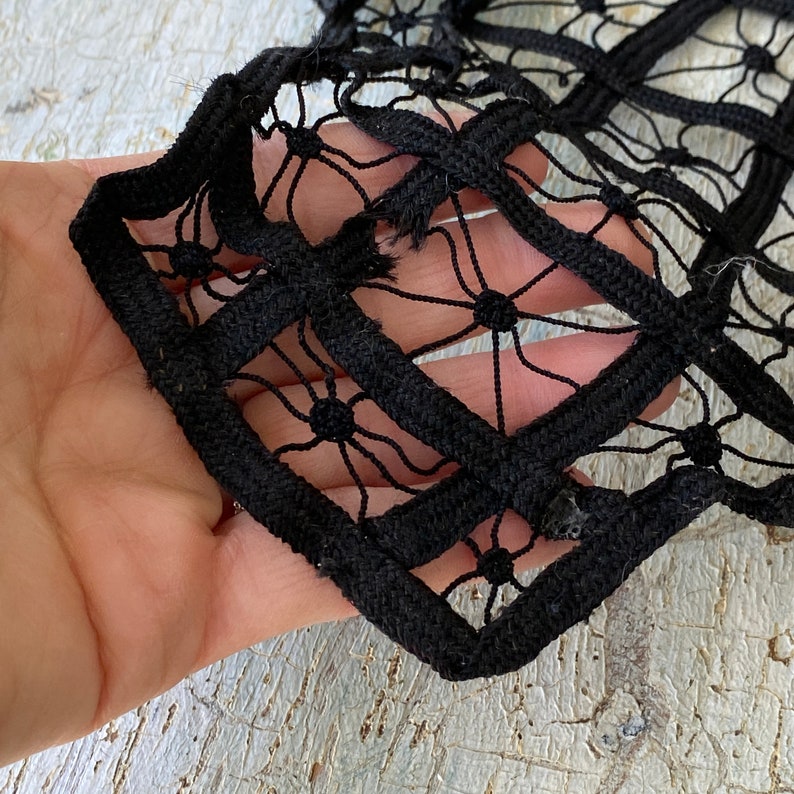 May include: Black lace fabric with a square pattern. The fabric is made of a thick, woven material and has a delicate, intricate design.
