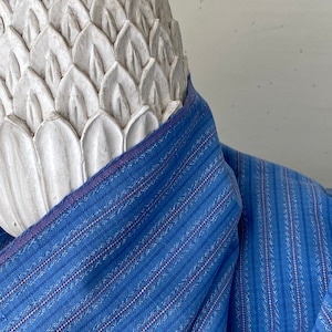 May include: A blue and white striped fabric with a textured surface. The fabric has a subtle pink stripe running through it.