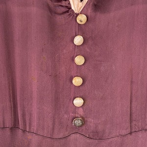 May include: A close-up of a purple silk dress with a row of six white buttons down the front.