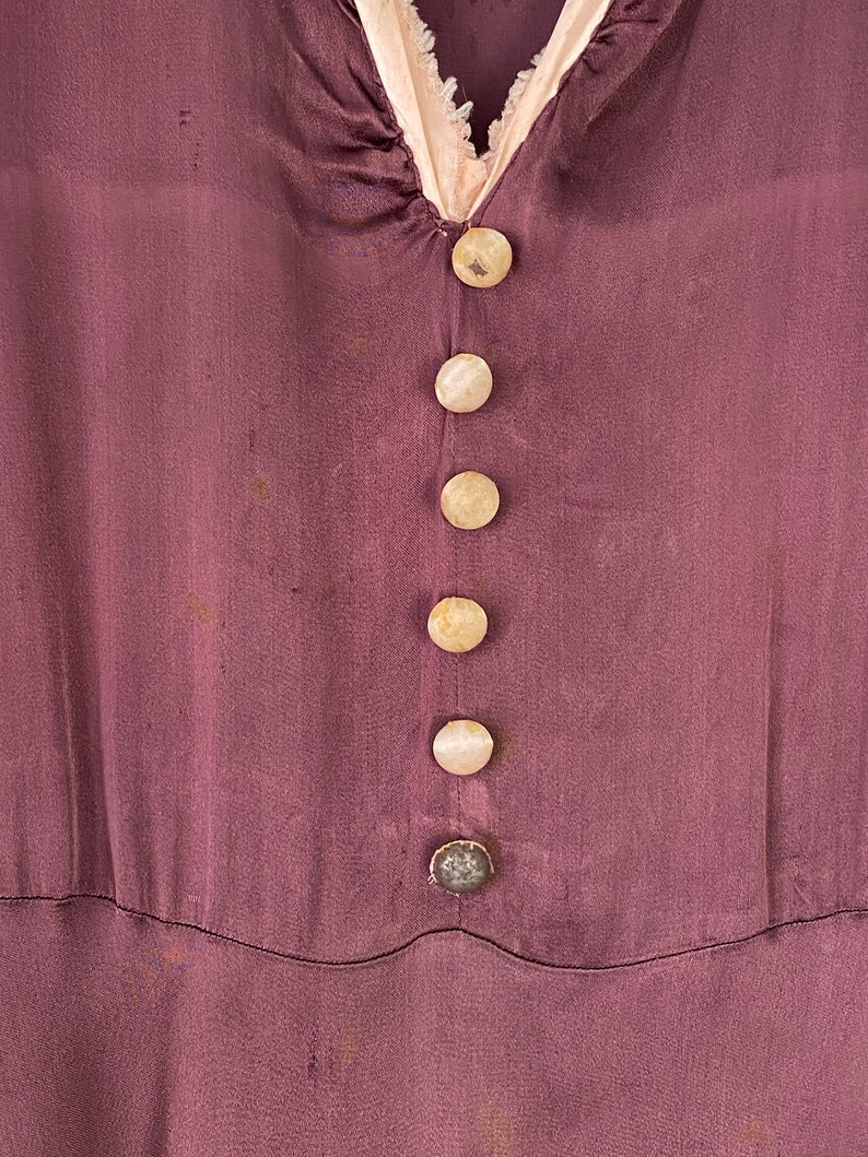 May include: A close-up of a purple silk dress with a row of six white buttons down the front.