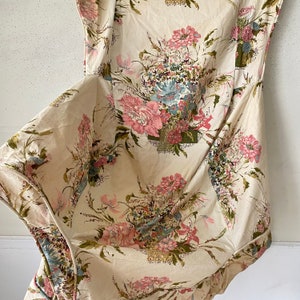 May include: A white fabric with a floral pattern featuring pink, green, and blue flowers. The fabric is crumpled and has a soft, textured look.
