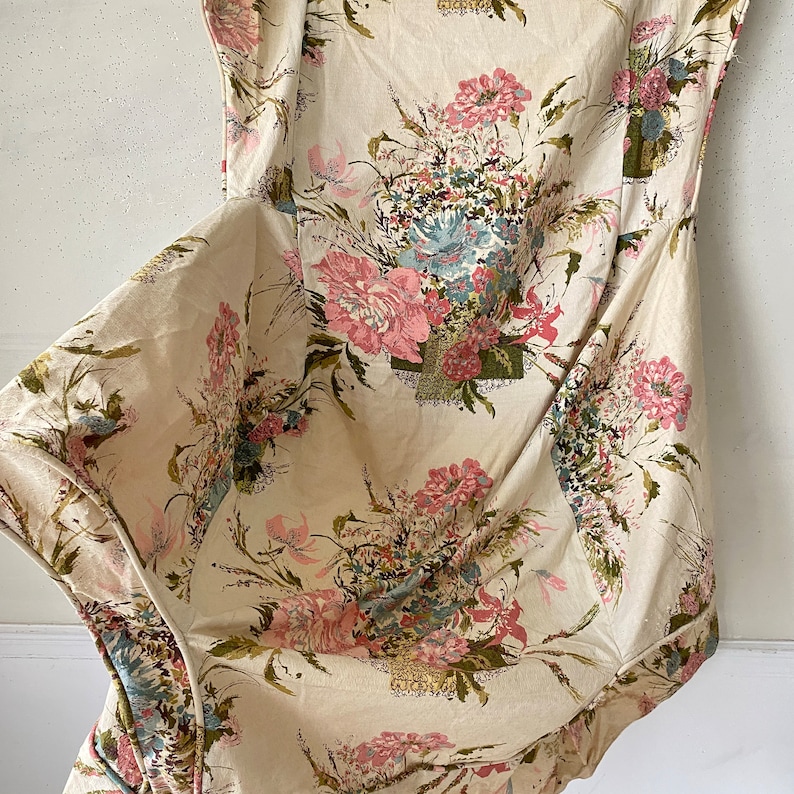 May include: A white fabric with a floral pattern featuring pink, green, and blue flowers. The fabric is crumpled and has a soft, textured look.
