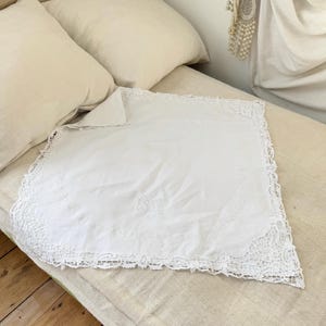 Könnte beinhalten: Weiße Tischdecke aus Baumwollspitze mit Stickereien. Die Tischdecke liegt auf einem weißen Bett mit Kissen.