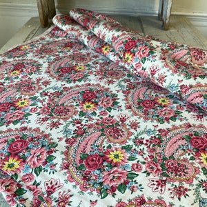 May include: A floral fabric with a paisley design. The fabric features a white background with a pattern of pink, red, yellow, and blue flowers. Two rolls of the fabric are visible, along with a flat section.