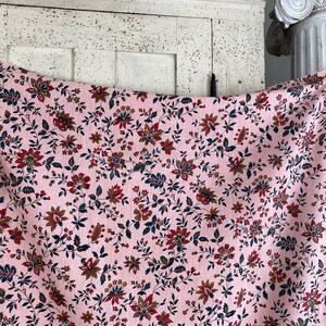 May include: Pink fabric with a floral pattern featuring small red and brown flowers on a white background.