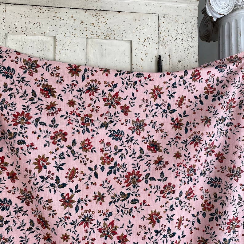 May include: Pink fabric with a floral pattern featuring small red and brown flowers on a white background.