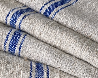May include: A stack of folded linen fabric with blue stripes. The fabric is a natural beige color and has a rough texture.
