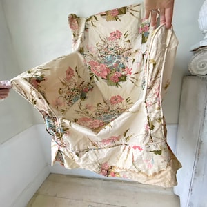 May include: A vintage floral fabric with a cream background and pink, blue, and green flowers. The fabric has a ruffled edge and is folded in half.