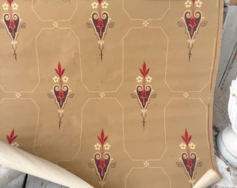 May include: A roll of antique wallpaper featuring a tan backdrop and a repeating design of burgundy, red, and cream floral elements. The pattern is enclosed by a light beige geometric outline. The wallpaper is partially unrolled, showing its aged texture.