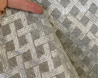 Può includere: Primo piano di un tessuto argento e grigio con un motivo geometrico. Il tessuto ha una lucentezza sottile e una superficie testurizzata.