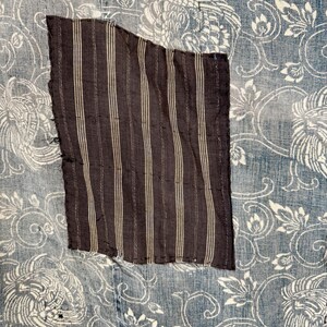 May include: A close-up of a blue and white fabric with a brown and white striped patch sewn on. The fabric has a floral pattern with a repeating design of stylized flowers and leaves.