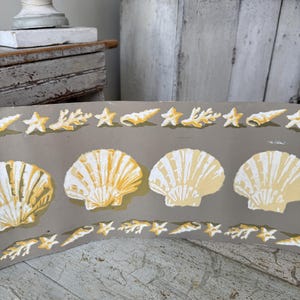 May include: A decorative border featuring a repeating pattern of yellow seashells, starfish, and coral on a gray background. The design has a vintage aesthetic, evoking a coastal or nautical theme.