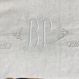 Puede incluir: Tela de lino blanco con un monograma bordado blanco de las letras "BP" en escritura cursiva. El monograma está rodeado de bordados decorativos.