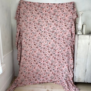 May include: A pink fabric with a floral print in shades of red, black, and white. The fabric is draped over a white surface.