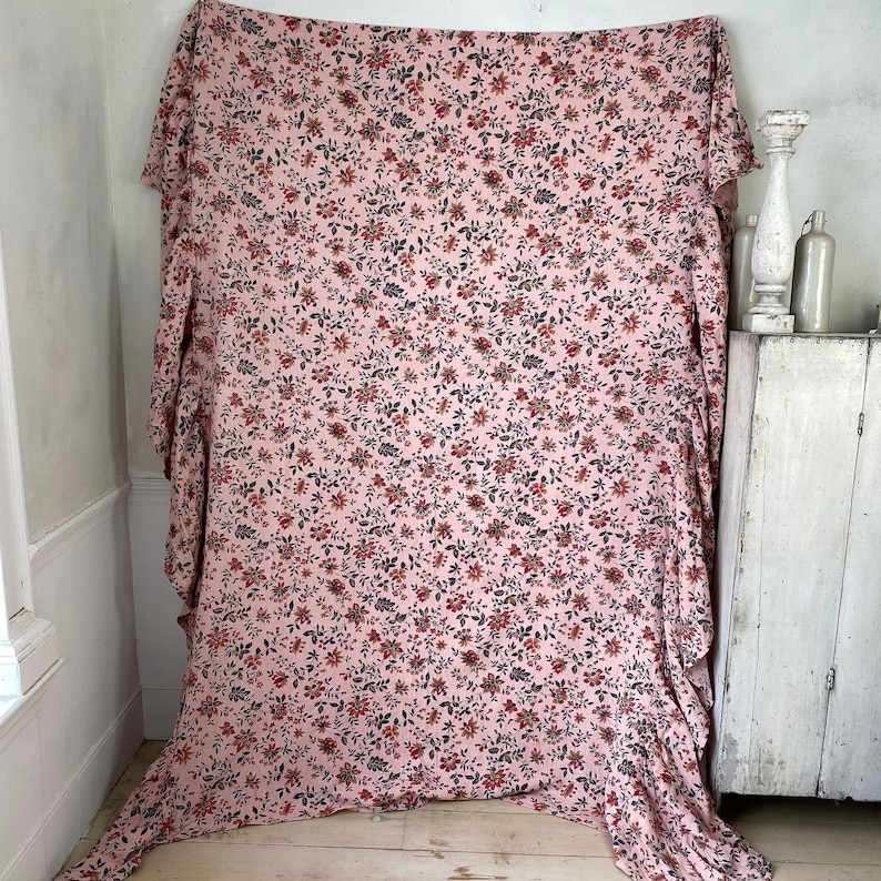 May include: A pink fabric with a floral print in shades of red, black, and white. The fabric is draped over a white surface.