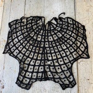 May include: Black lace shawl with a circular design. The lace is delicate and intricate, creating a spiderweb-like pattern.