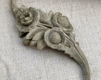 May include: A gray, carved, floral design with three round, raised details. The design is reminiscent of a stylized flower or leaf.