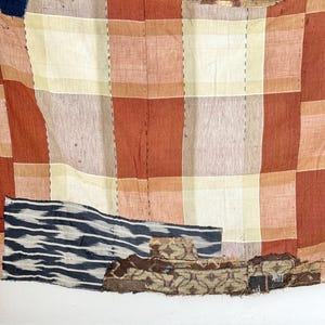 May include: A vintage patchwork quilt with a red, white, and brown checkered pattern. The quilt is made of different fabrics and has been repaired with patches. The quilt is faded and worn, showing signs of age and use.