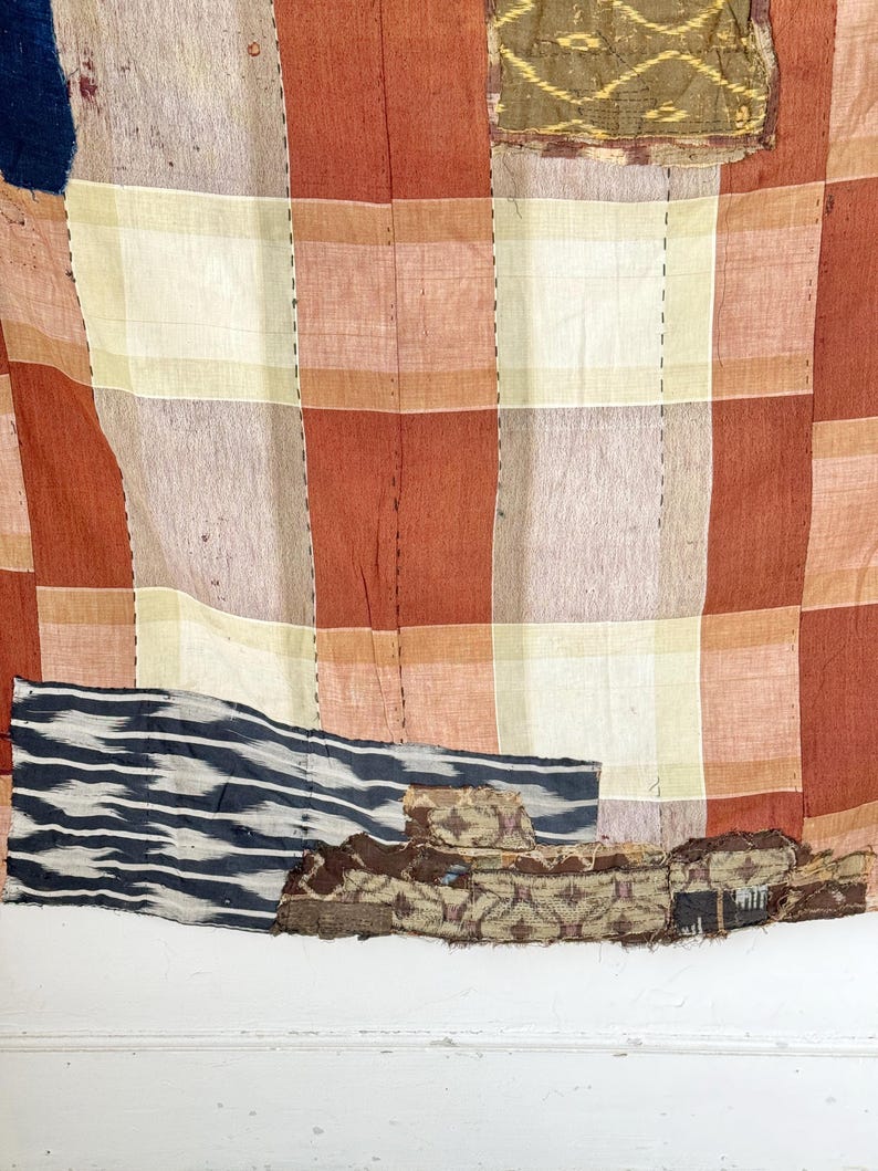May include: A vintage patchwork quilt with a red, white, and brown checkered pattern. The quilt is made of different fabrics and has been repaired with patches. The quilt is faded and worn, showing signs of age and use.