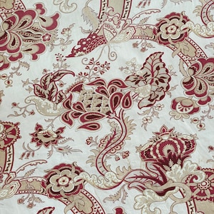 Könnte beinhalten: Ein beigefarbener Stoff mit einem sich wiederholenden Muster aus burgunderroten und cremefarbenen Blumendesigns. Das Muster zeigt komplizierte Wirbel und Blätter.