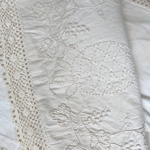 May include: White cotton tablecloth with a delicate lace border and embroidered grapevine design.