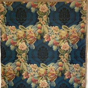 May include: A blue fabric with a repeating pattern of pomegranates, flowers, and leaves. The fabric has a textured, woven look.