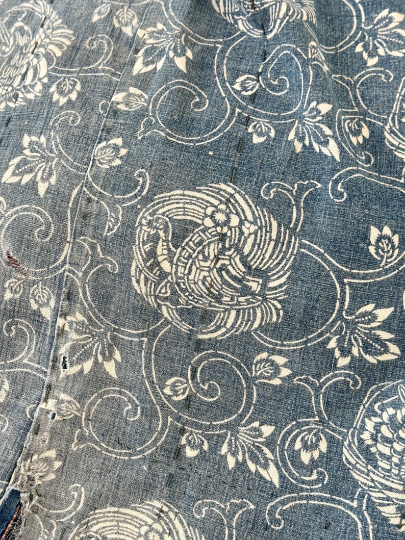 May include: Close-up of a blue fabric with a white floral pattern. The pattern features stylized flowers and birds.