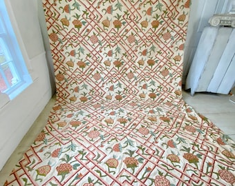 May include: A large piece of fabric with a repeating pattern of pink and orange flowers on a white background. The flowers are surrounded by a green lattice design.