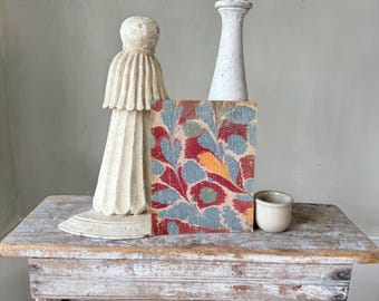 Può includere: Una panca rustica in legno con finitura bianca anticata supporta una collezione di oggetti vintage. Una statua bianca scolpita, una colonna bianca, una piccola tazza in ceramica e un blocco a motivi floreali rossi, blu e gialli sono esposti.
