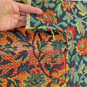 May include: Close-up of a black fabric with a colorful floral pattern. The fabric has a woven texture and features red, yellow, green, and pink flowers.