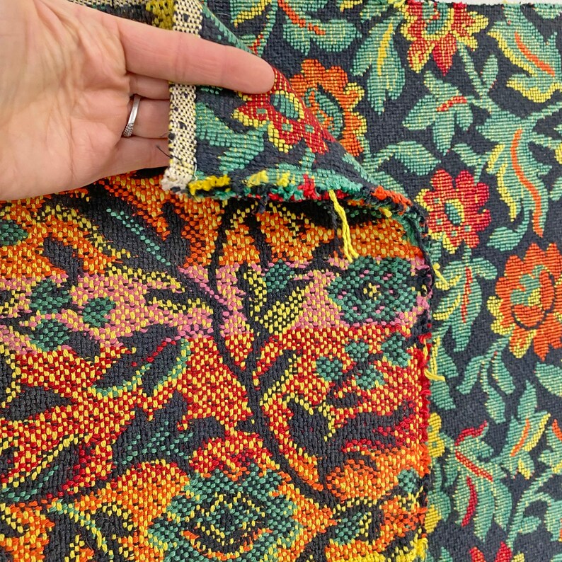 May include: Close-up of a black fabric with a colorful floral pattern. The fabric has a woven texture and features red, yellow, green, and pink flowers.