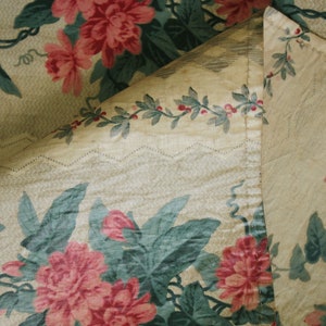 K&ouml;nnte beinhalten: Nahaufnahme eines Stoffes mit Blumenmuster. Der Stoff ist hellbeige mit einem gr&uuml;nen und rosafarbenen Blumendesign. Der Stoff ist &uuml;ber sich selbst gefaltet und zeigt einen hellbeigen Stoff mit einem gr&uuml;nen Rankenmuster.