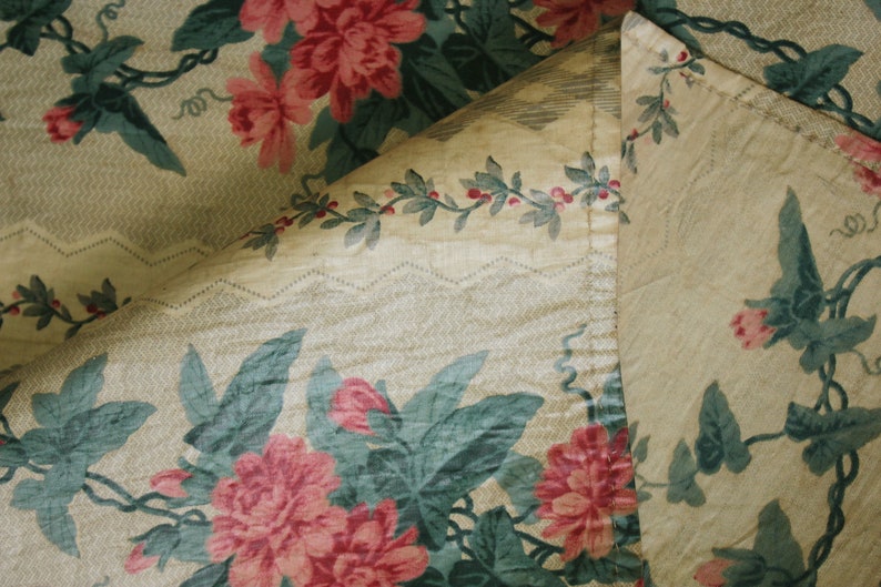 K&ouml;nnte beinhalten: Nahaufnahme eines Stoffes mit Blumenmuster. Der Stoff ist hellbeige mit einem gr&uuml;nen und rosafarbenen Blumendesign. Der Stoff ist &uuml;ber sich selbst gefaltet und zeigt einen hellbeigen Stoff mit einem gr&uuml;nen Rankenmuster.