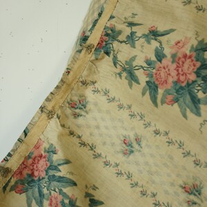 K&ouml;nnte beinhalten: Nahaufnahme eines beigefarbenen Stoffes mit Blumenmuster. Der Stoff zeigt rosa Rosen mit gr&uuml;nen Bl&auml;ttern und Ranken. Der Stoff hat einen hellbeigen Hintergrund mit einem dezenten Karomuster.