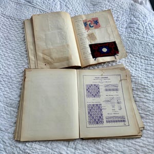 Pode incluir: Dois livros antigos abertos sobre um fundo branco. O livro superior tem uma amostra de tecido vermelho, azul e branco com um desenho de estrela. O livro inferior tem uma p&aacute;gina intitulada "PIQUE LOSANGE" e um diagrama de um padr&atilde;o de ponto.